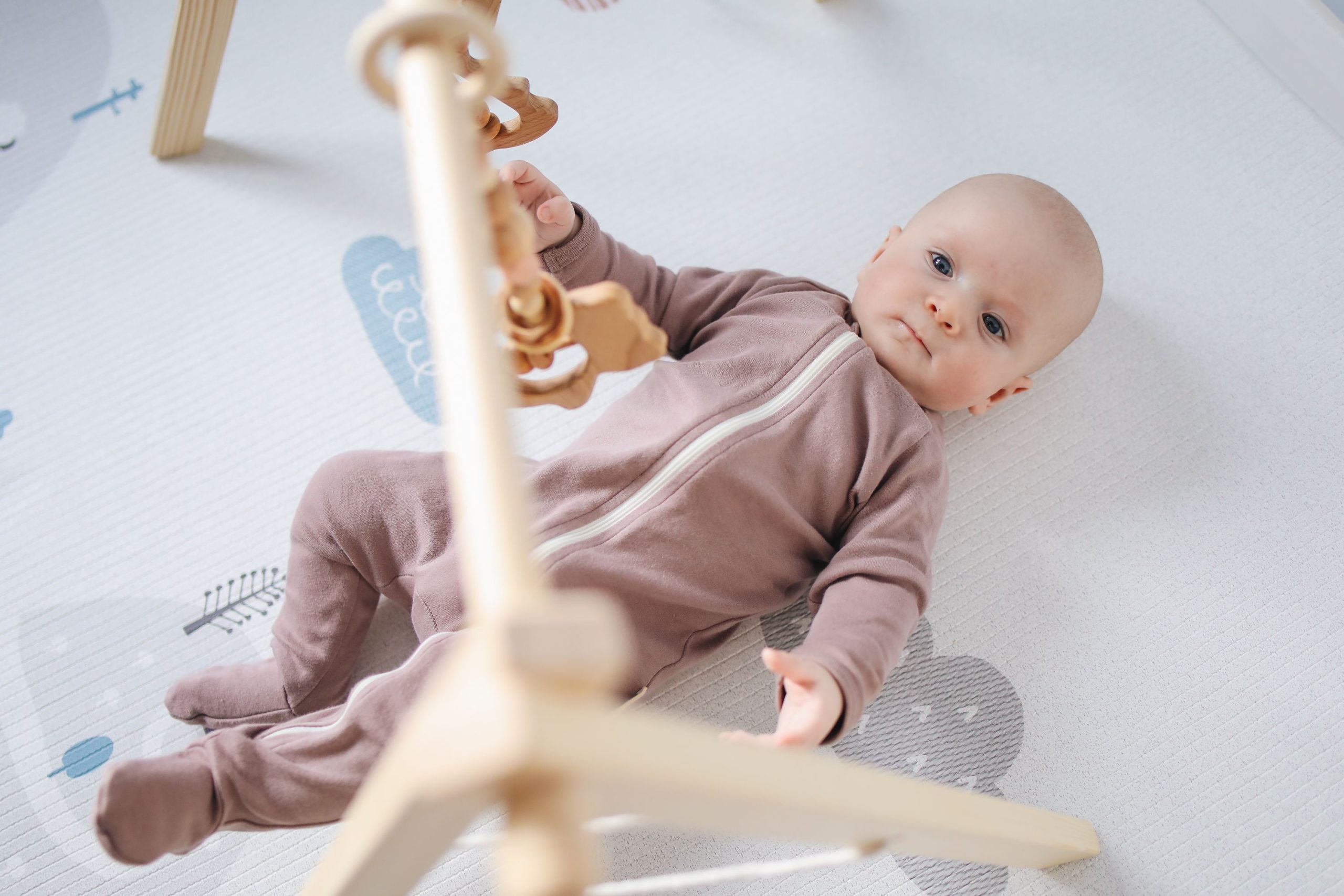 Cute baby in a cozy onesie playing with wooden toys on a soft mat indoors.